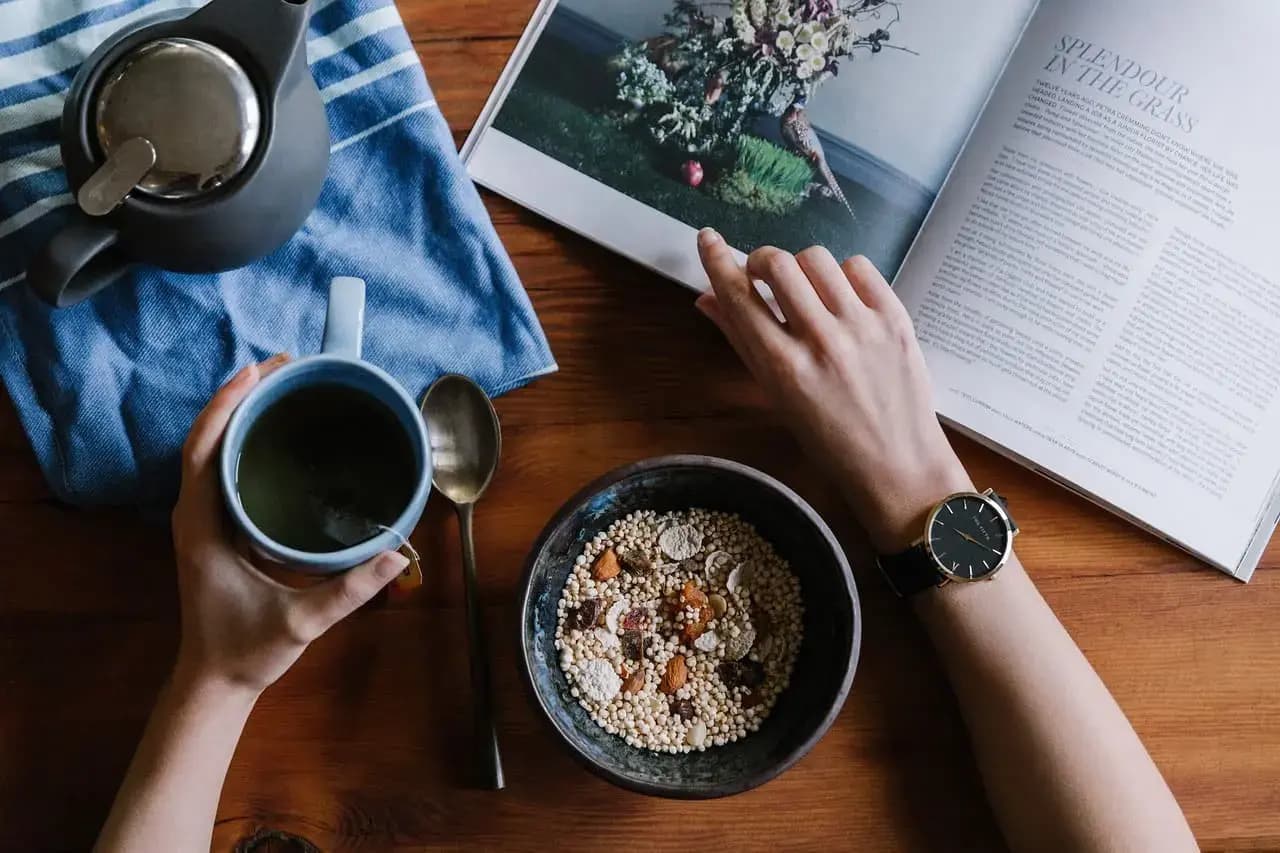 Healthy person reading while drinking a hot drink, with oats and healthy food